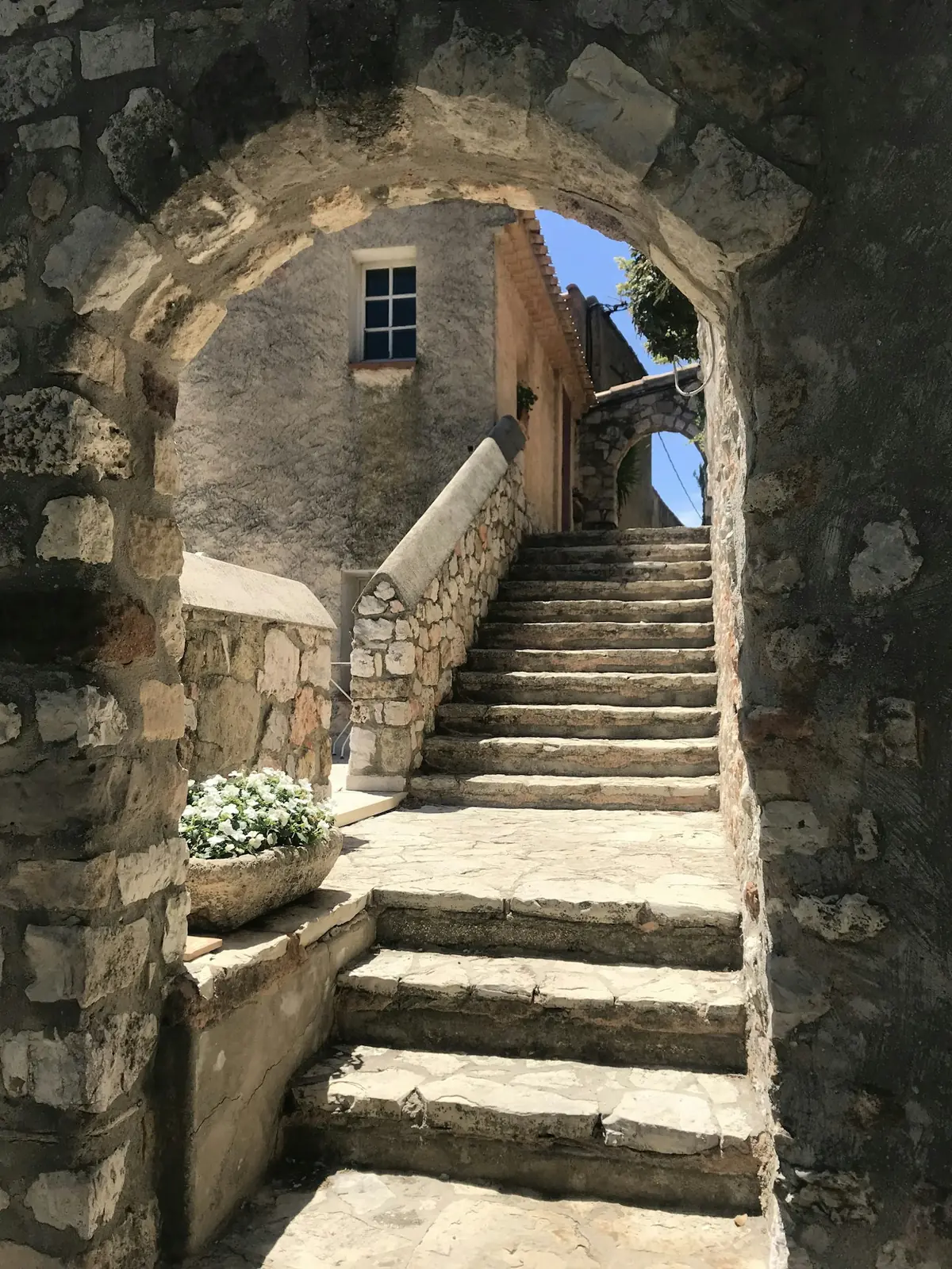 Escalier de pierre sous une arche, vers une cour lumineuse